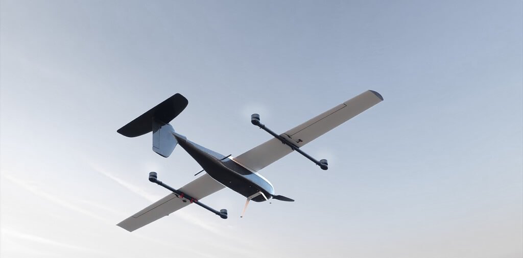 A small drone aircraft with four propellers is flying against a clear sky.