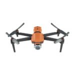 Orange quadcopter drone with a camera, featuring four propellers and an aerodynamic design, viewed from the front on a white background.