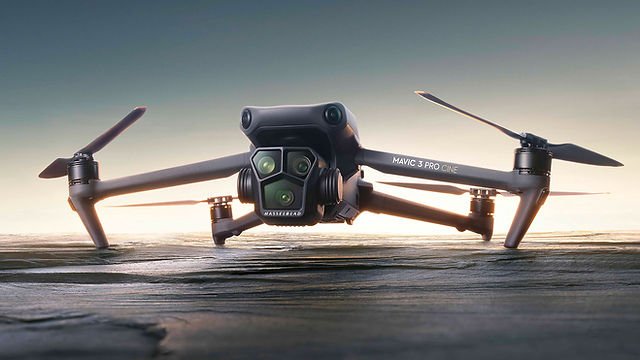 A drone with four propellers hovers close to the ground against a blurred background.