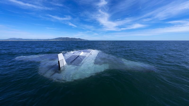 Partially submerged sailboat in a calm sea under a blue sky with distant mountains in the background.