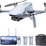 A white drone with propellers, remote control displaying a mountain image, two batteries, and a black carrying case.