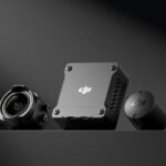 DJI camera components on a dark surface, including a camera lens, square module, and cylindrical cap.