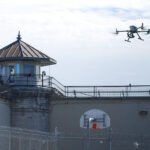 A drone flies near a prison watchtower under a cloudy sky.