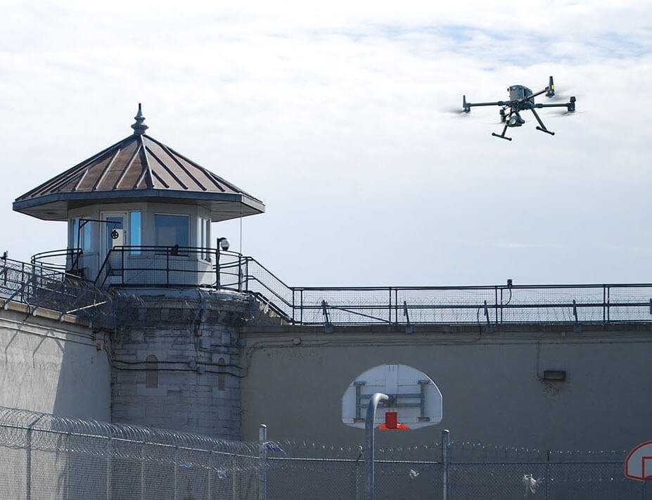 A drone flies near a prison watchtower under a cloudy sky.