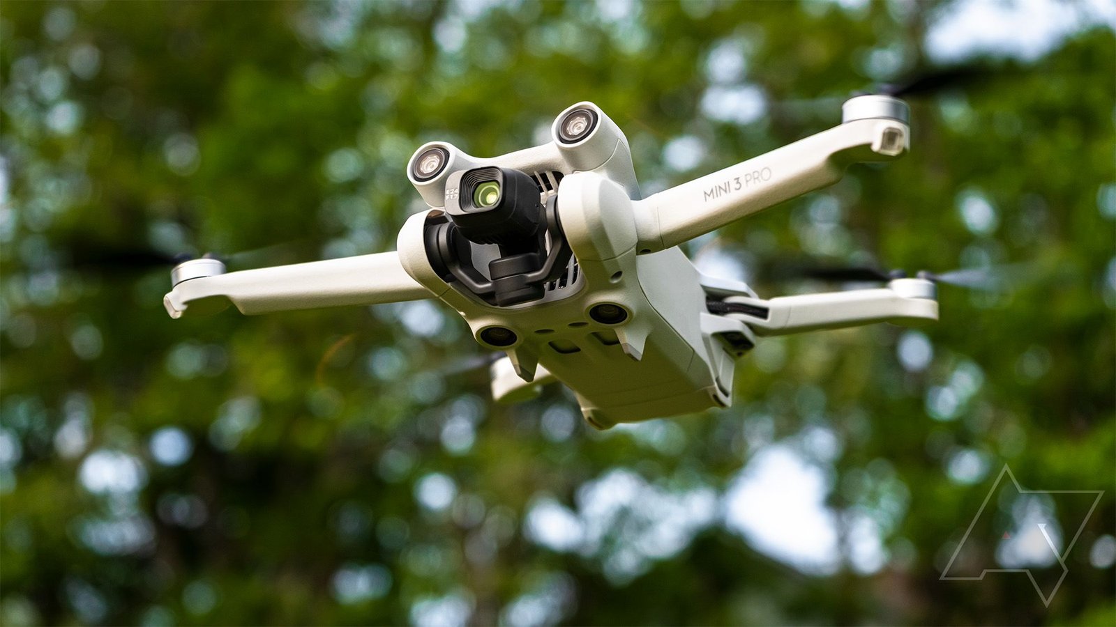 A small drone flying outdoors against a blurred green leafy background.