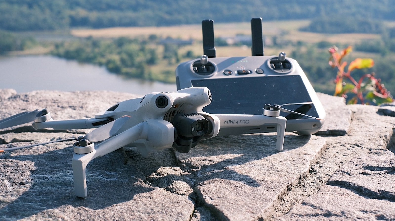 A drone and its remote controller are placed on a rocky surface with a blurred landscape in the background.