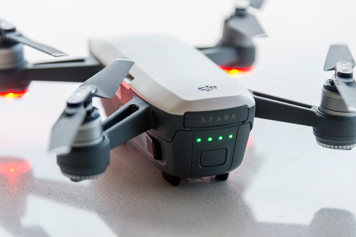 Close-up of a DJI Spark drone on a surface, showing its front LEDs lit in green and propellers extended.