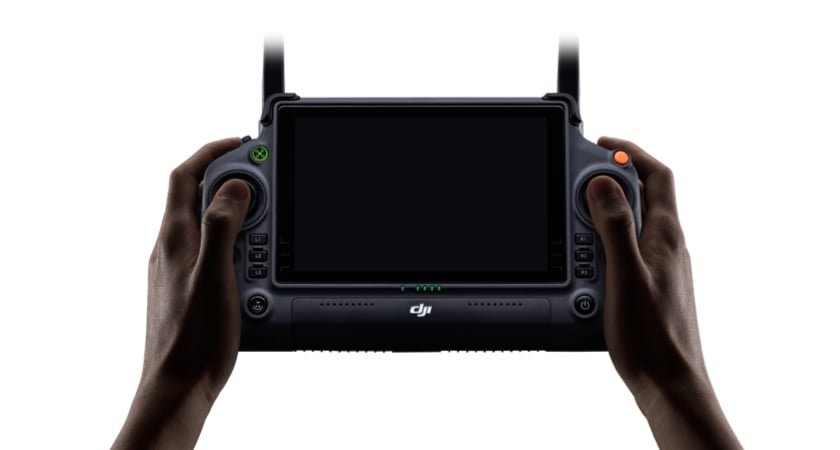 Hands holding a DJI remote controller with a screen, featuring buttons and antennas on each side.