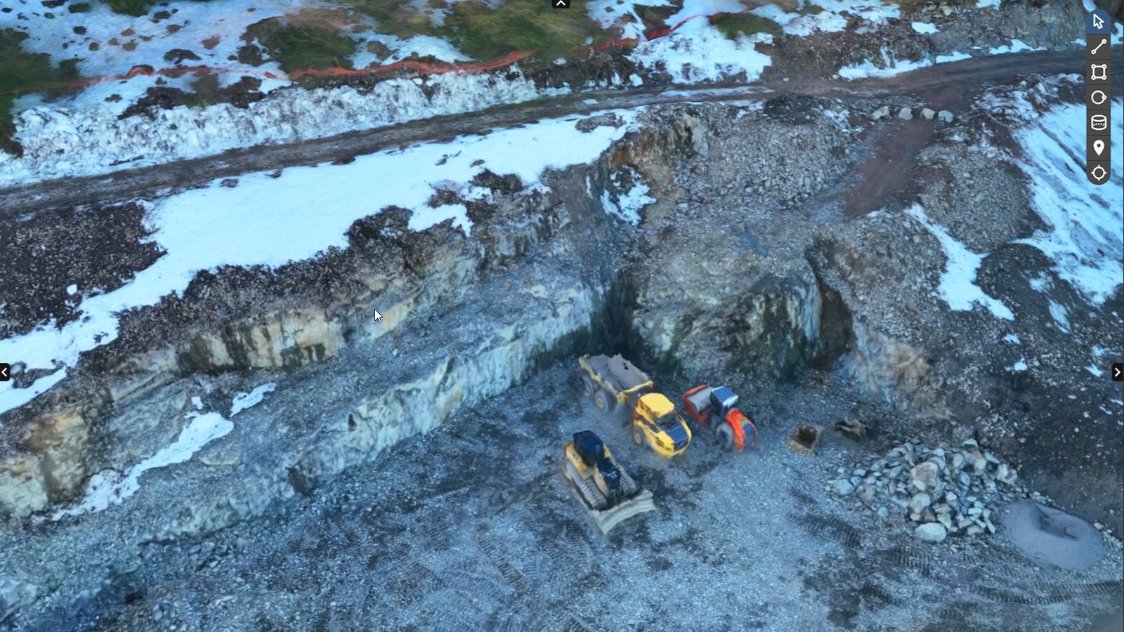 Aerial view of construction site with machinery on gravel, surrounded by snow and rocky terrain.