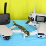 Two drones with propellers are displayed on a blue surface alongside two remote controllers, one black and one white. The background is green.