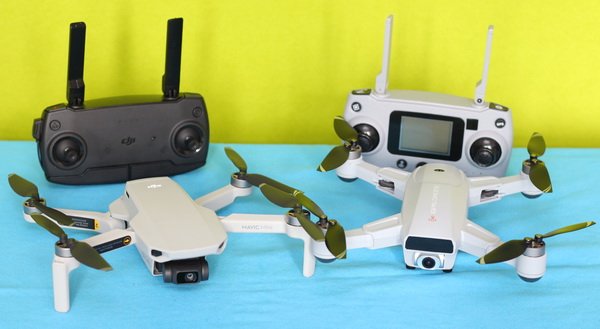 Two drones with propellers are displayed on a blue surface alongside two remote controllers, one black and one white. The background is green.