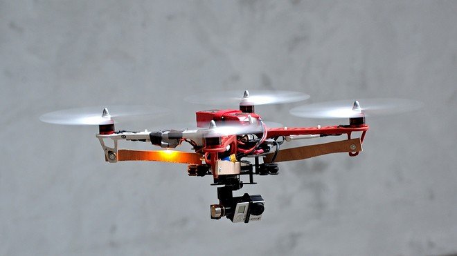 A red and white drone with four propellers hovers in the air against a gray background.