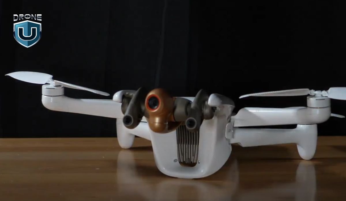 A white drone with four propellers and a camera is on a wooden surface. A "Drone U" logo is in the top left corner.