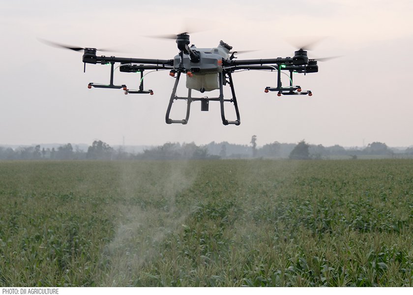 A drone sprays crops in a field under an overcast sky.