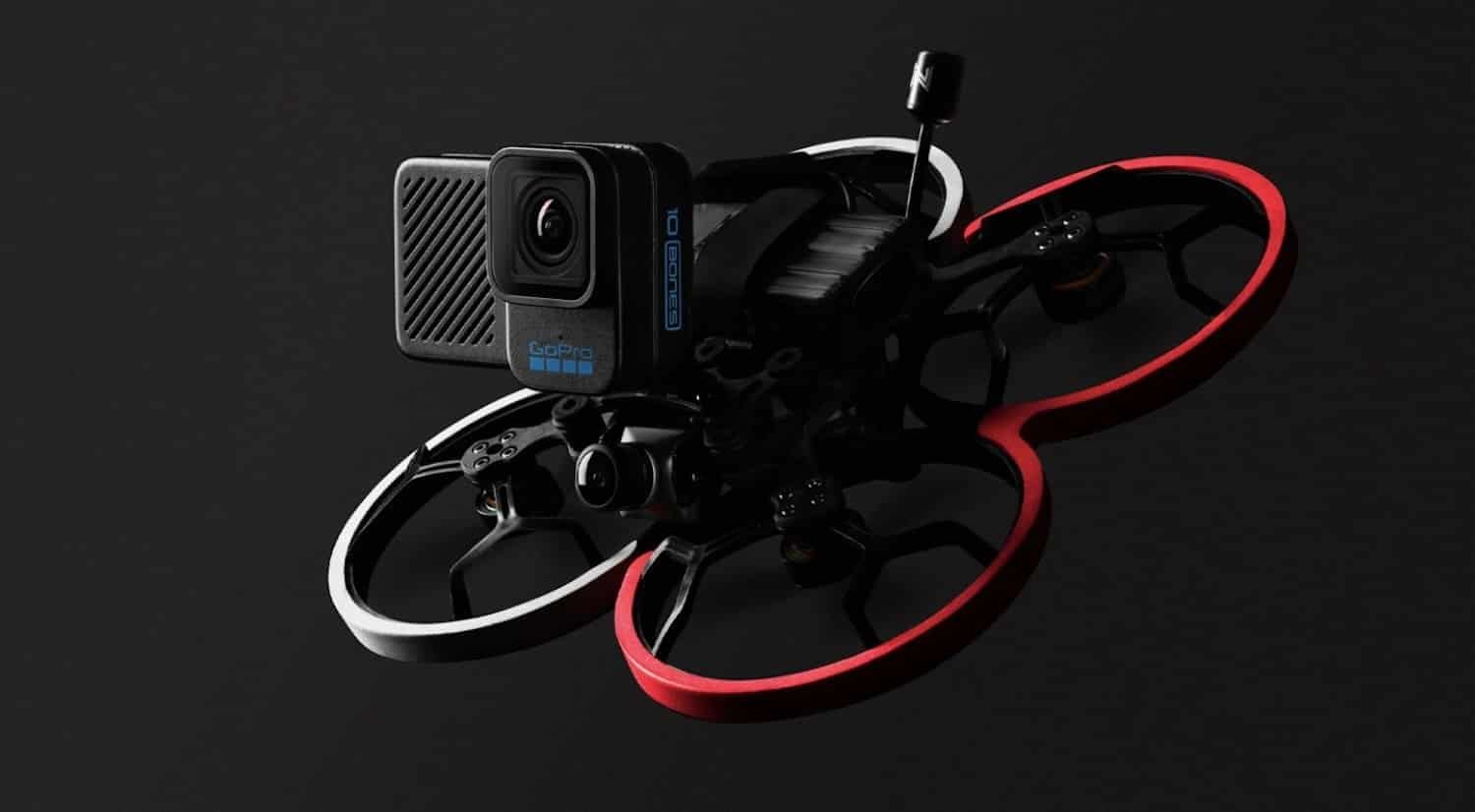 A small drone with three propellers, featuring red and white guards, is equipped with a camera, set against a dark background.