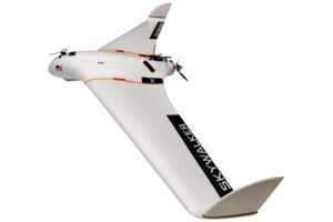 White Skywalker UAV with a sleek, fixed-wing design and propeller, featuring an American flag decal and the word "SKYWALKER" on the wing.