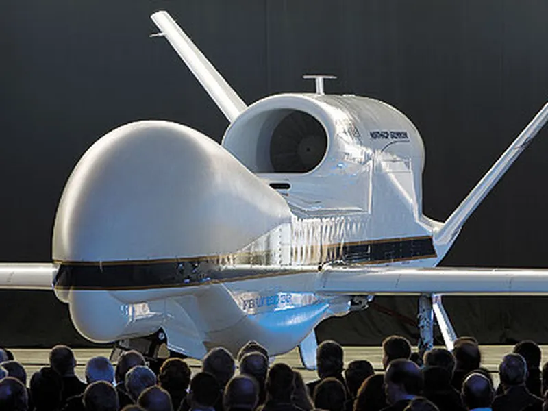 A large drone aircraft displayed indoors with a crowd of people observing it.