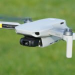 A white quadcopter drone is flying over a grassy field.