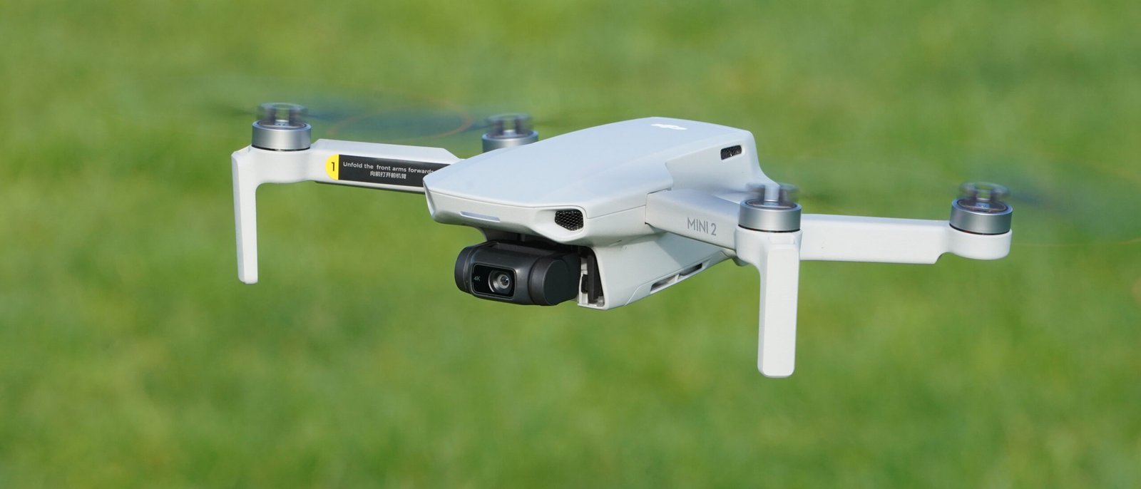 A white quadcopter drone is flying over a grassy field.