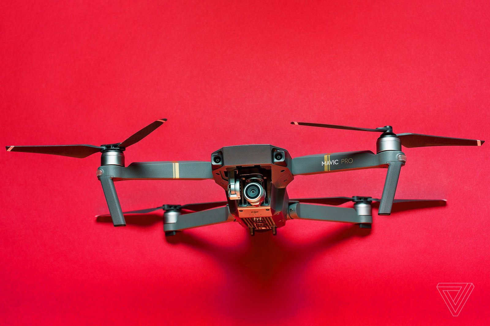 A drone with extended propellers is positioned against a solid red background.