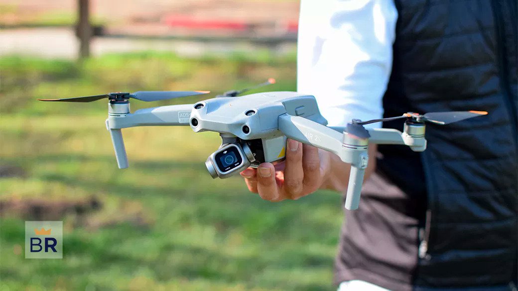 A person holding a small white drone outdoors, featuring four propellers and a camera.