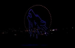 A display of blue lights forms the outline of a dolphin jumping through a circular arrangement of lights against a dark background.