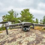 Drone positioned on a rocky surface outdoors, surrounded by trees.