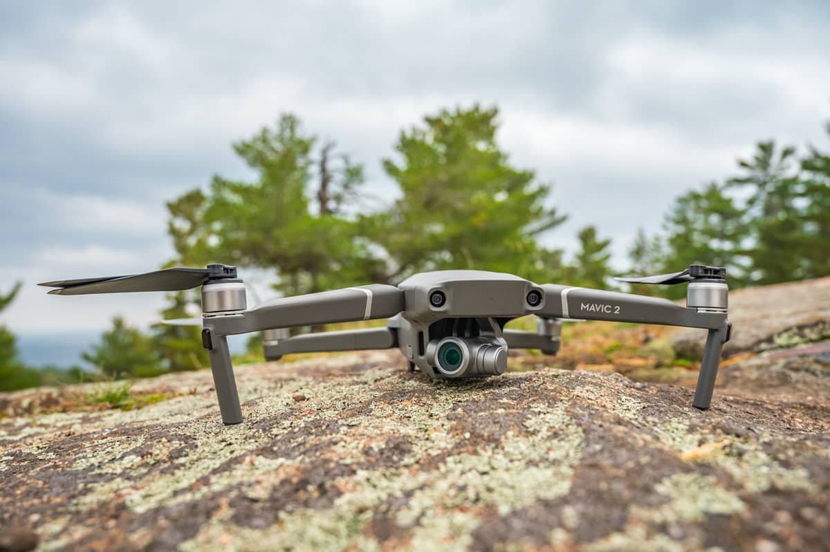 Drone positioned on a rocky surface outdoors, surrounded by trees.