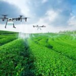 Drones spraying a green, terraced field under a cloudy sky.