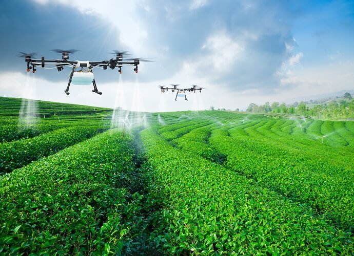 Drones spraying a green, terraced field under a cloudy sky.