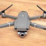 A gray DJI Mavic 2 drone with four propellers and a camera is placed on a wooden floor.