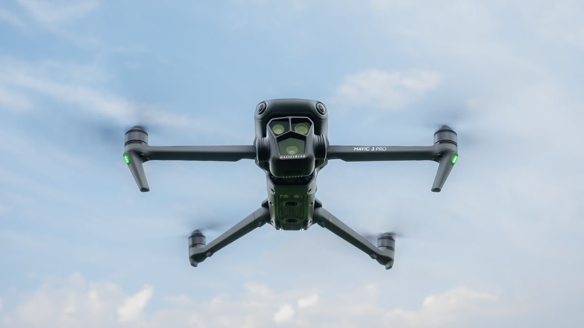 A black quadcopter drone flying in the sky with four propellers spinning.