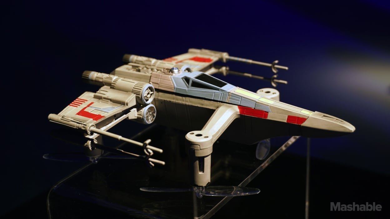 A model of a sci-fi spaceship with wings and laser cannons, displayed under a spotlight on a dark background.