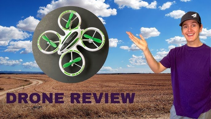 Person gesturing at a green and white drone with a rural landscape in the background. Text reads "Drone Review.