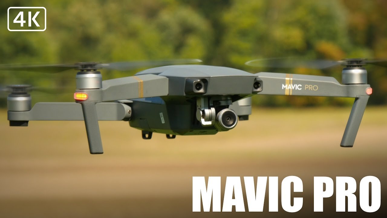 A Mavic Pro drone hovering outdoors with spinning rotors. "Mavic Pro" and "4K" text are visible on the image. Trees and grass are in the background.