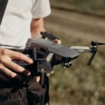 A person holding a gray drone outdoors, preparing it for flight.