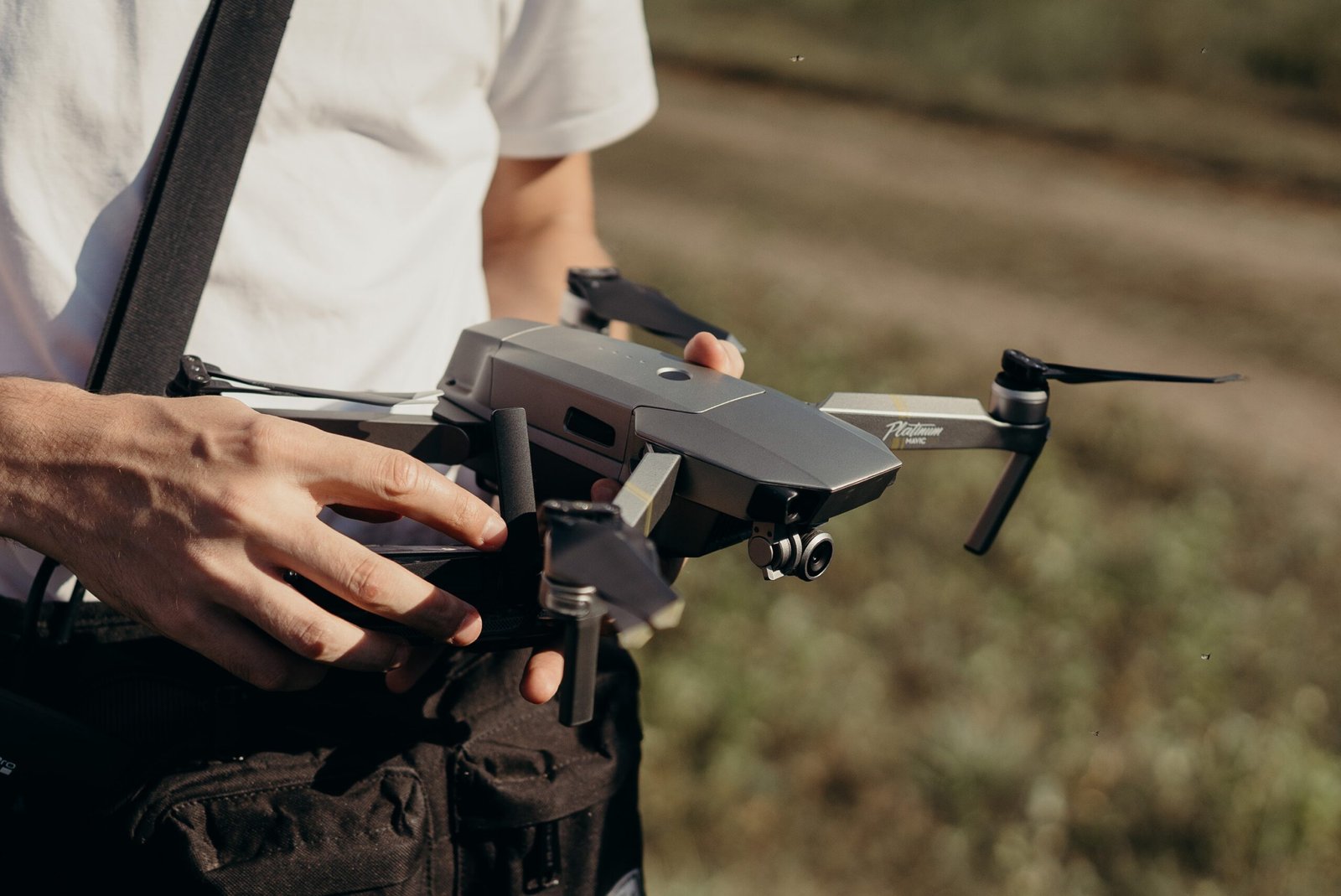 A person holding a gray drone outdoors, preparing it for flight.