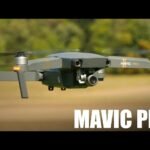 A Mavic Pro drone flying outdoors with a blurred background of trees and grass.